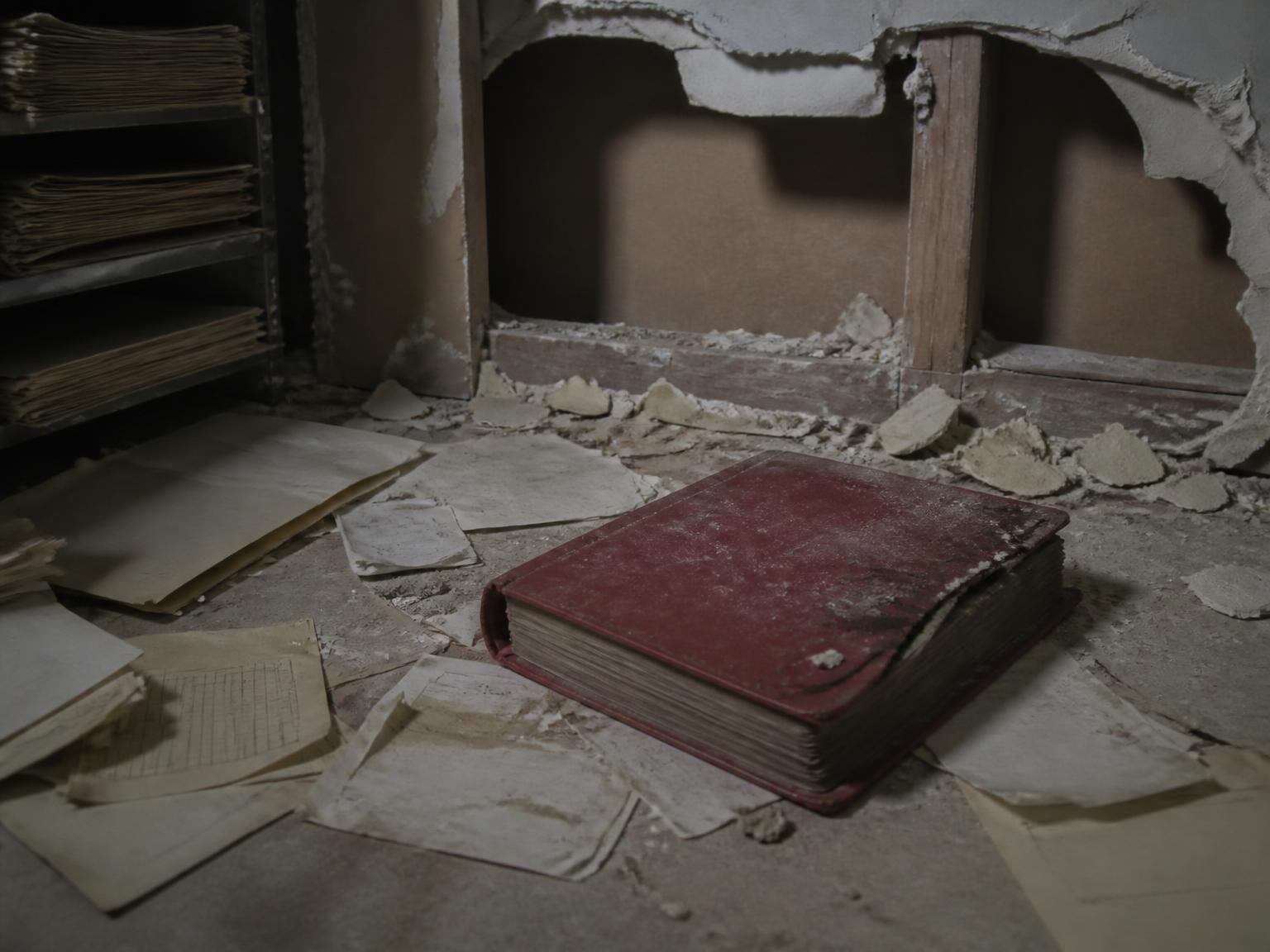A damaged red ledger among papers in a dim basement records archive